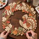 Hands painting the fall Welcome wreath with a cheerful turkey at a craft table