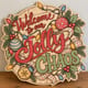 Painted round Welcome to Our Jolly Chaos sign standing on a wooden table