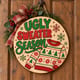 Painted round Ugly Sweater Season sign hanging on a wooden front door