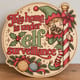 Painted round This Home Is Under Elf Surveillance sign standing on a wooden table