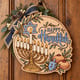 Painted round Happy Hanukkah sign with a menorah and dreidel hanging on a wooden front door
