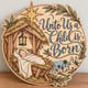 Painted round Unto Us a Child Is Born sign with baby Jesus in a manger standing on a wooden table