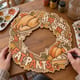 Hands painting the Hope You Wore Your Fat Pants Thanksgiving wreath at a craft table