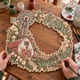 Hands painting the Home Sweet Home farmhouse wreath with a barn and windmill at a craft table
