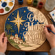 Hands painting the round Oh Holy Night sign with the Star of Bethlehem at a craft table