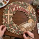 Hands painting the nativity Merry Christmas wreath with baby Jesus and a cross at a craft table