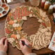 Hands painting the Hello Fall pumpkin and wheat wreath at a craft table