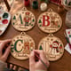Hands painting personalized alphabet Christmas ornaments at a craft table