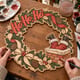 Hands painting the Ho Ho Ho Santa chimney wreath at a craft table