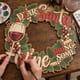 Hands painting the Dear Santa Bring Some Wine wreath at a craft table