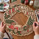 Hands painting a Christmas Trees Cut and Carry wreath with a red vintage truck and green pines