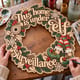 Hands painting the This Home Is Under Elf Surveillance wreath at a craft table