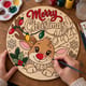 Hands painting the round reindeer Merry Christmas sign with string lights at a craft table