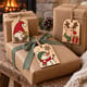 Painted gnome, snowman and reindeer gift tags on presents by a fireplace