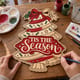 Hands painting the Tis the Season Christmas tree door hanger at a craft table