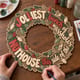 Hands painting the Christmas lights wreath with humorous jolliest bunch nuthouse lettering at a craft table